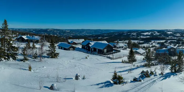 Utsiktsbilde fra Ølnesseter Hyttegrend på vinteren. Man ser flere hytter med fjellandskap i bakgrunn